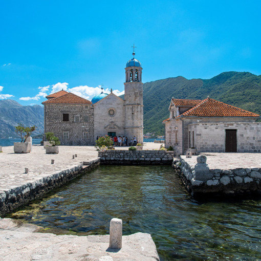 Stone church and buildings on a small island waterfront with mountains in the background