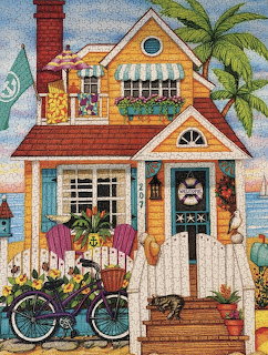 Yellow beach cottage with turquoise door, striped awning, white picket fence, bicycle, and palm tree