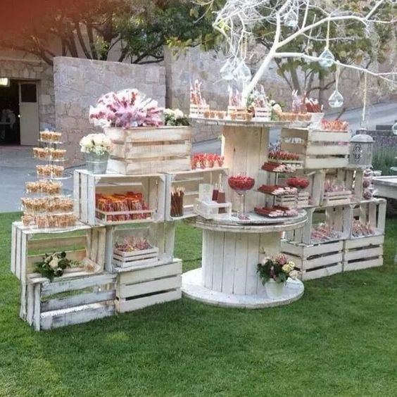White wooden crate dessert display with cupcakes and flowers on grass in outdoor garden