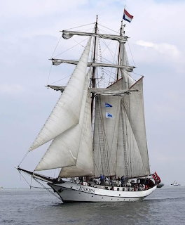 Tall ship with white sails and Dutch flag sailing on calm grey sea under overcast sky