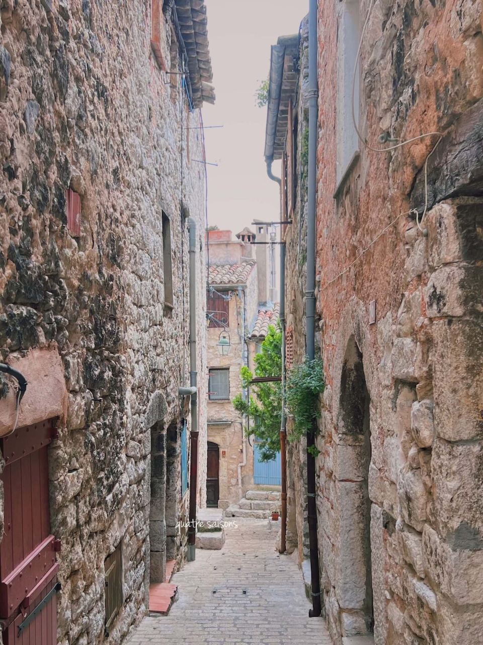 Narrow cobblestone alley between old stone walls in a French village with wooden door and distant greenery