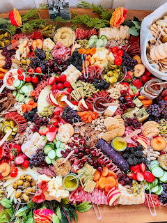 Overhead view of abundant grazing board with fruits, cheeses, crackers, nuts, and flowers on wooden table
