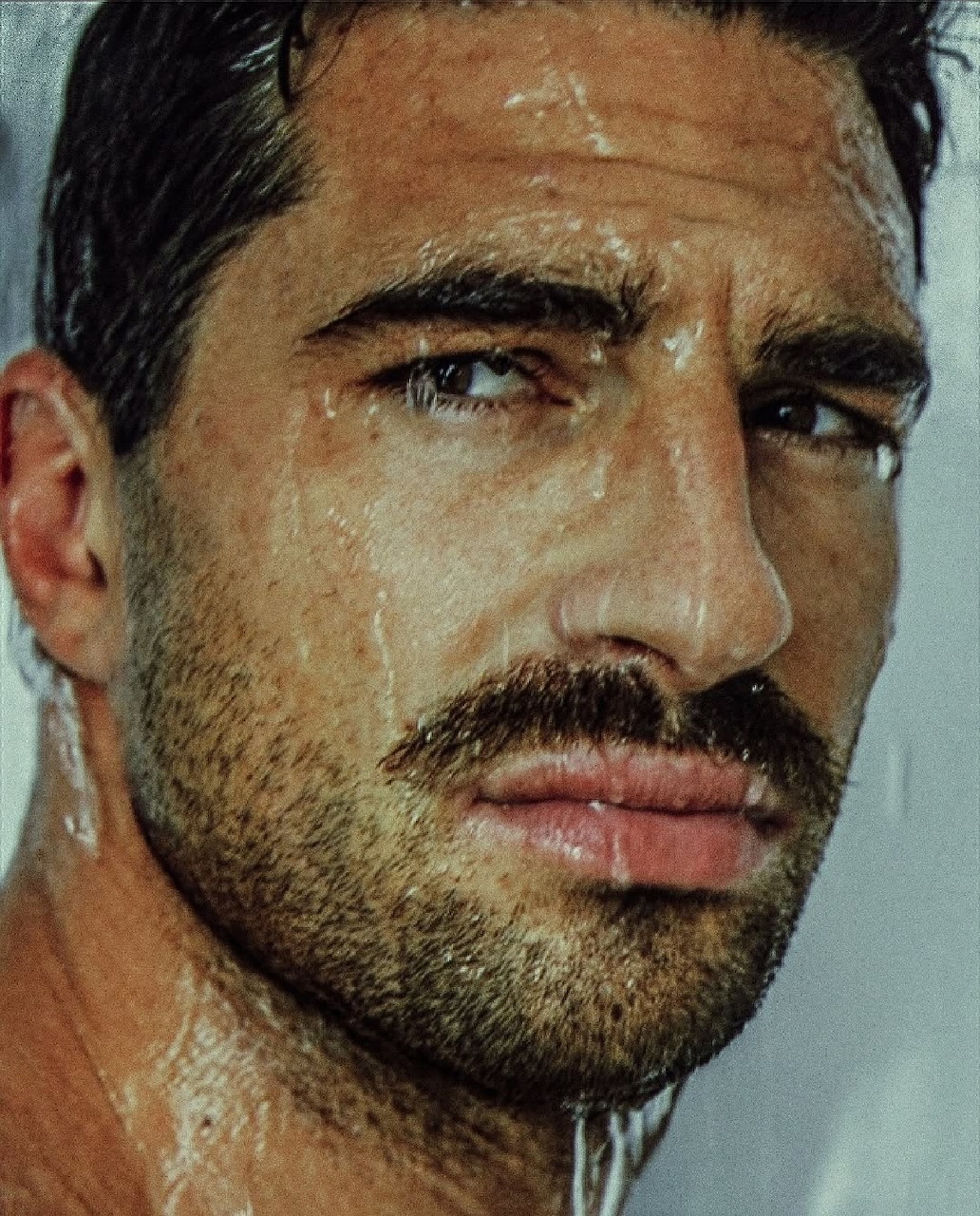 Close-up of a man's wet face with moustache and water droplets