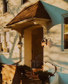 Rustic wooden door with pitched canopy, lanterns, and potted plants on sunny cottage entrance