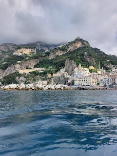 Coastal town with colorful buildings at base of green rocky mountains viewed from the sea
