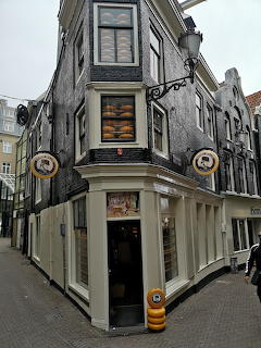 Old gray corner building on a narrow Amsterdam street with hanging signs and tall windows