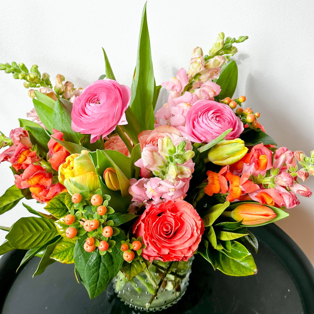 Colorful flower bouquet with pink roses, yellow tulips, and orange berries in green vase