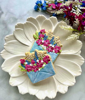 Blue envelope cookie with pink, yellow, and gold floral icing on white flower plate