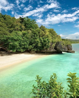 Turquoise tropical lagoon with white sand beach, limestone cliffs, and lush green trees under blue sky