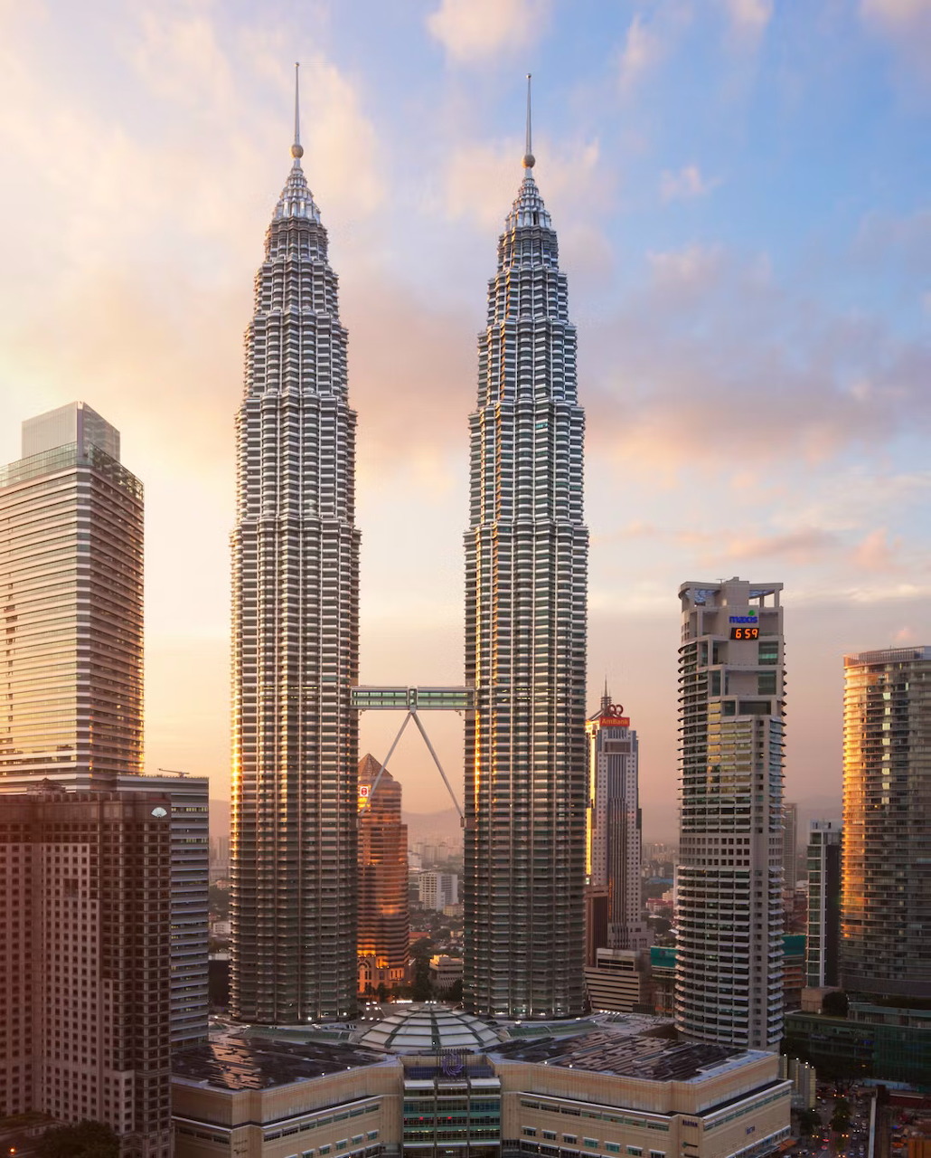 Petronas Twin Towers in Kuala Lumpur at sunset with nearby city skyscrapers