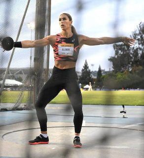 Woman athlete winding up to throw a discus inside a throwing cage outdoors
