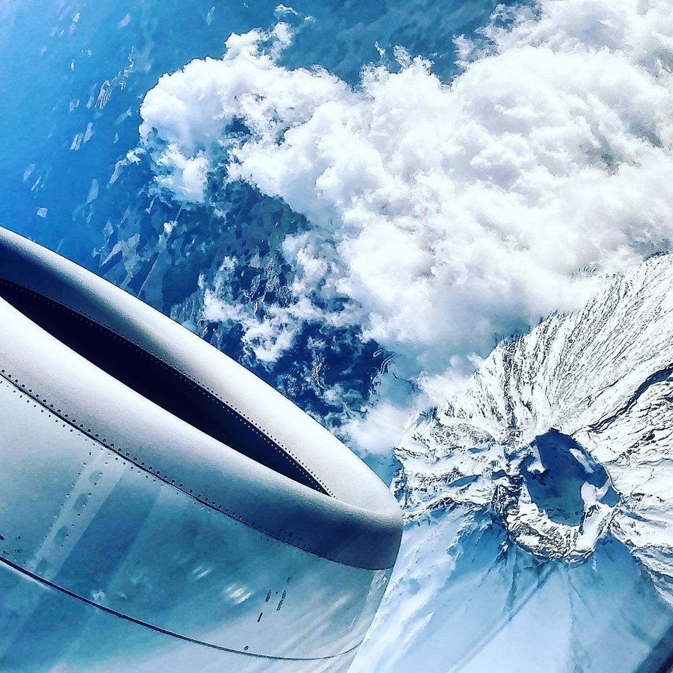 Airplane view of snow-covered Mt. Fuji and clouds with part of the engine visible