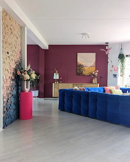 Modern living room with blue velvet sofa, burgundy accent wall, pink flower pedestal, and stone block wall