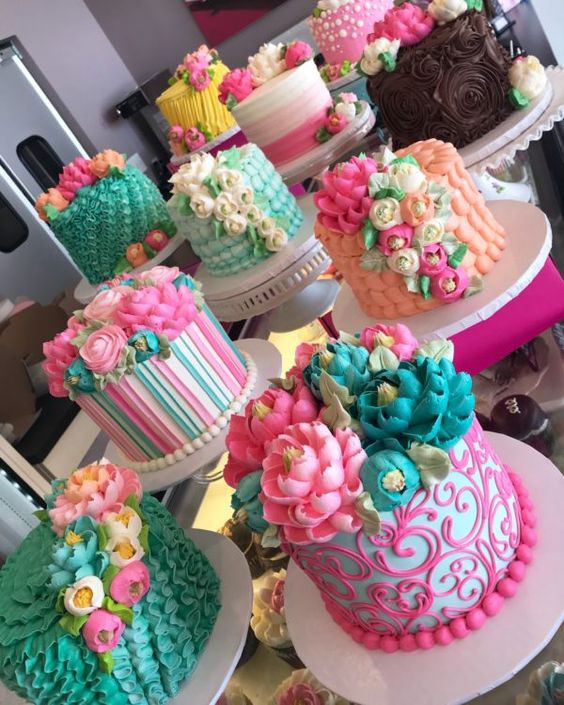 Colorful decorated cakes with frosting flowers and fondant designs on white cake stands