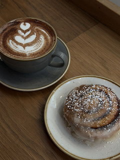 Cappuccino with leaf latte art and glazed cinnamon roll dusted with powdered sugar on wooden table