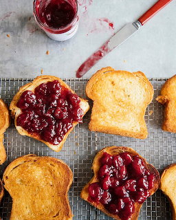 Toast slices spread with sour cherry preserves on a wire cooling rack, with a jam jar and knife above.