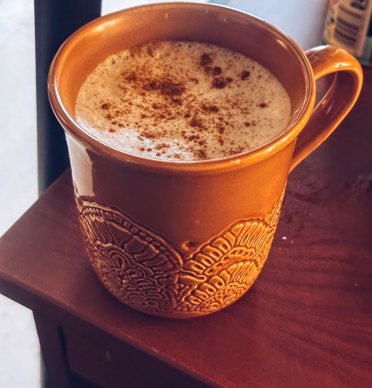 Orange mug with leaf pattern holding frothy chai latte with cinnamon sprinkled on top