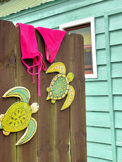 Pink bikini top hanging on a wooden fence beside two colorful turtle decorations