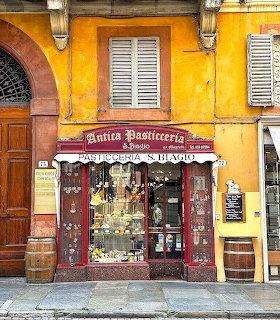 Facade of Antica Pasticceria S. Biagio with yellow walls and red-framed display window in Modena, Italy