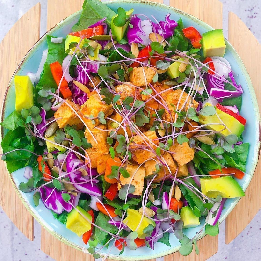 Top view of a fresh salad with mixed vegetables, purple cabbage, microgreens, and orange dressing in a white bowl