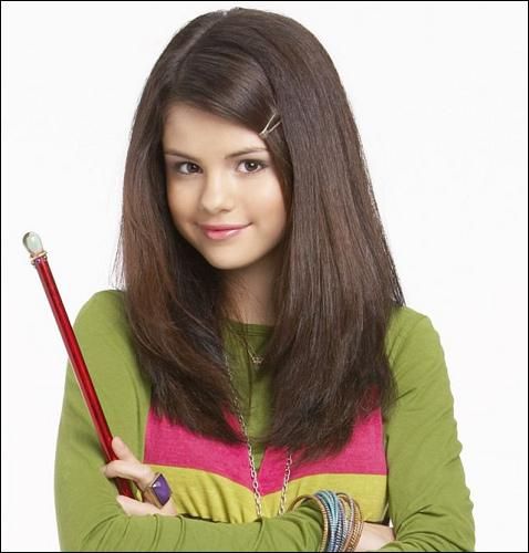 Smiling young woman with long dark hair holding a red wand against a plain background