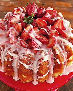 Bundt cake with white icing drizzle and fresh strawberry topping on red plate
