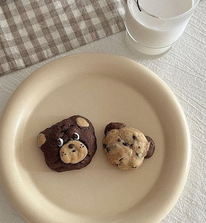 Two bear-shaped cookies on a beige plate with a glass of milk and checkered tablecloth