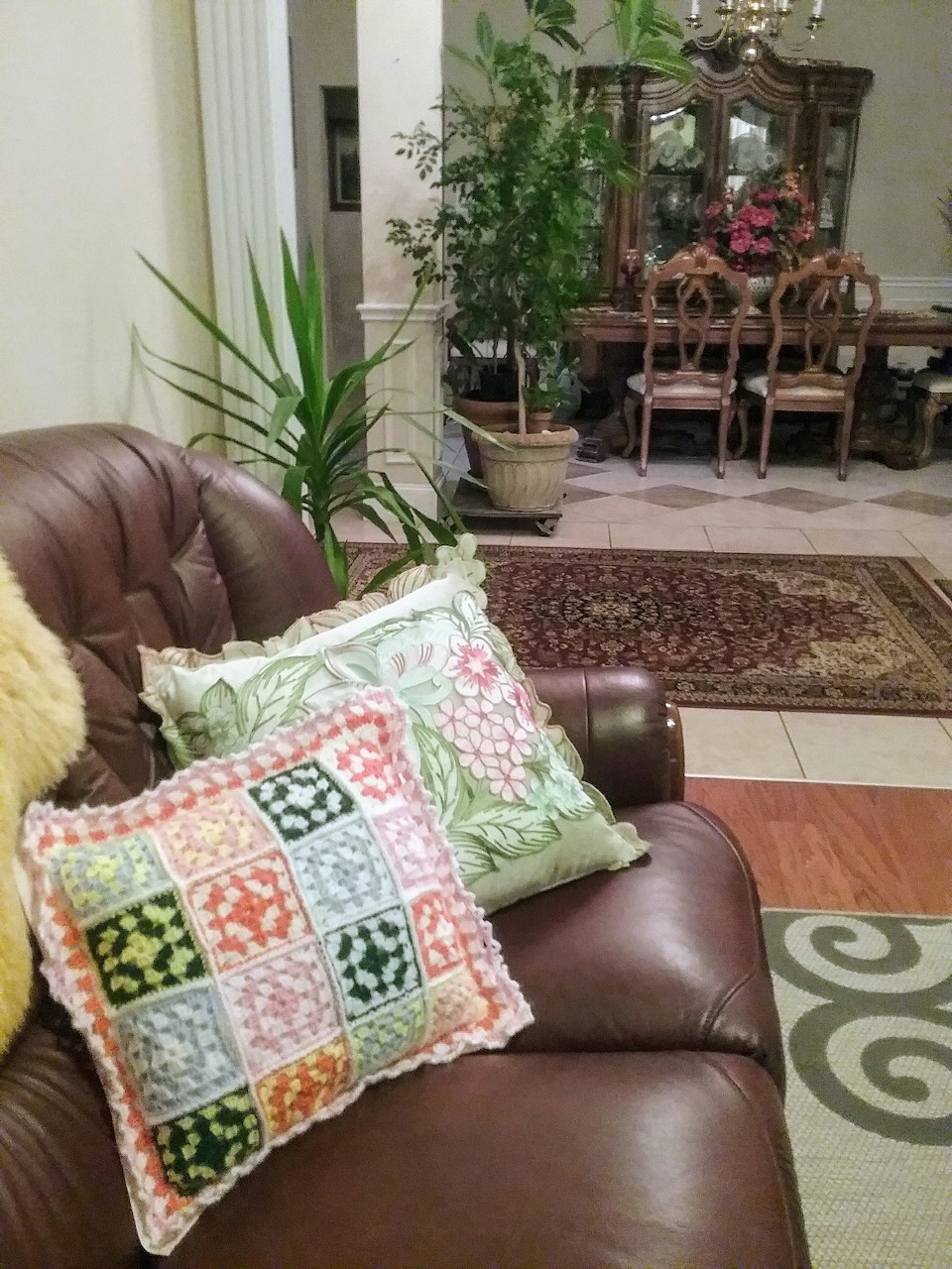 Two colorful handmade quilted pillows on brown leather chair in home interior