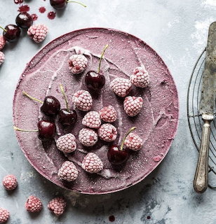 Pink cheesecake topped with raspberries and cherries on a decorative plate with vintage spoon