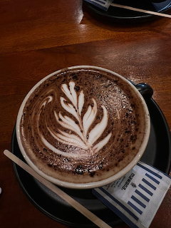 Latte with white leaf foam art in cup on wooden table