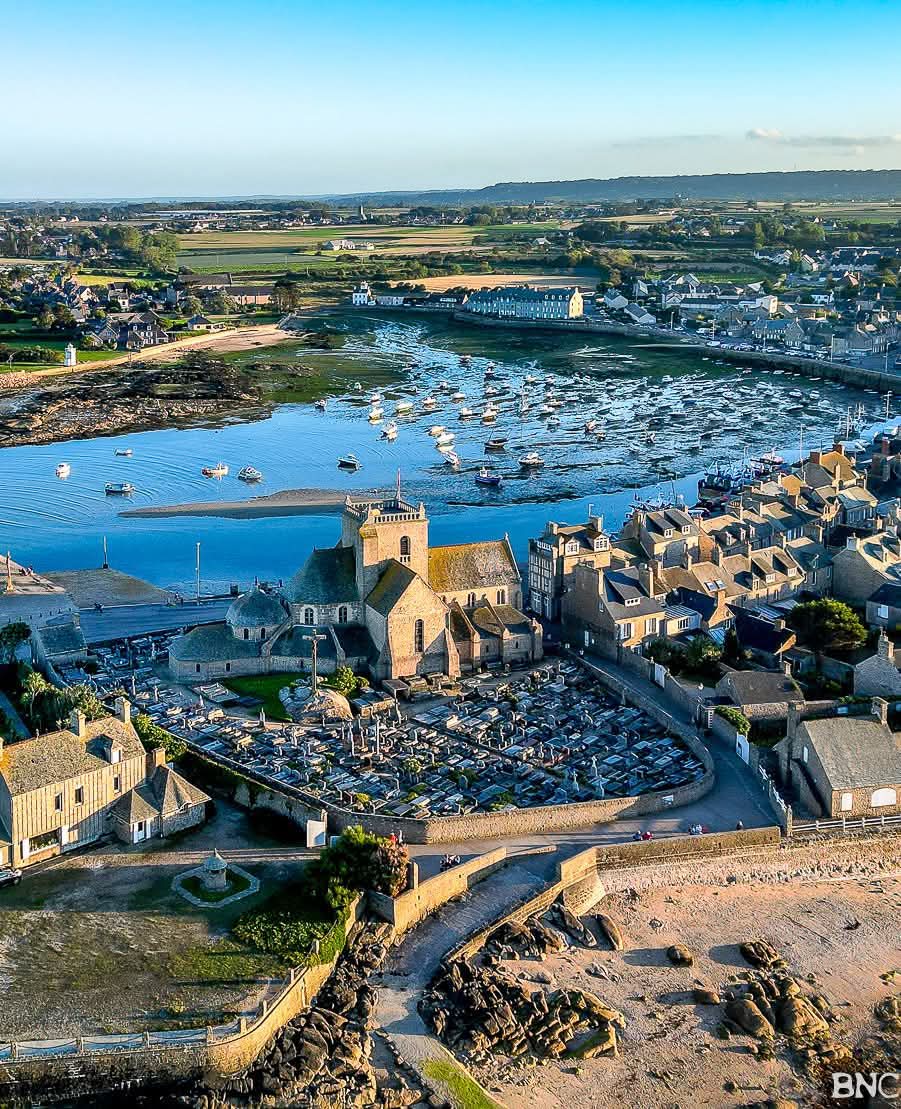 Aerial view of a historic coastal town with harbor, stone buildings, church, and boats at low tide
