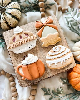 Decorated autumn cookies shaped like pumpkins and acorns on a wooden board with fall decorations