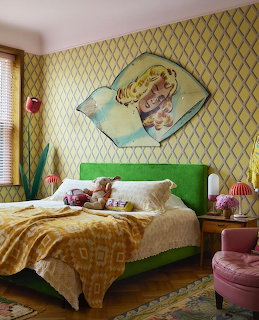 Colorful eclectic bedroom with green bed, yellow patterned wallpaper, and vintage artwork above headboard