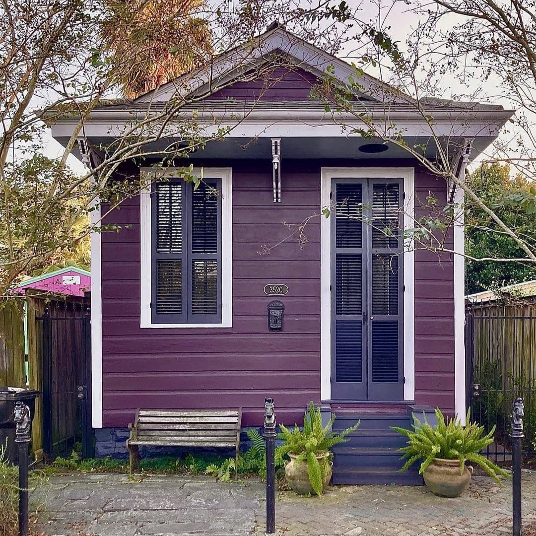 Purple tiny house with white trim, porch, and potted plants in front