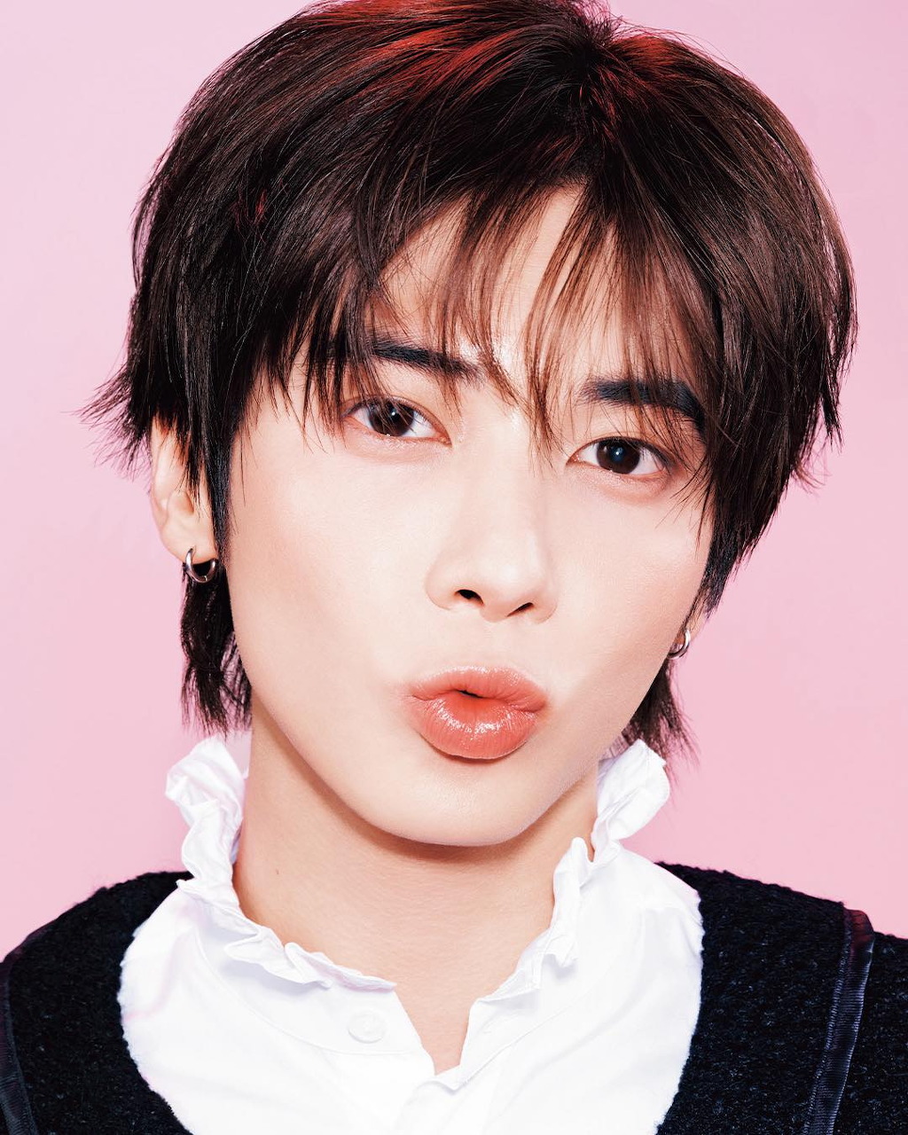 Young man with dark hair and ear stud posing against a pink background