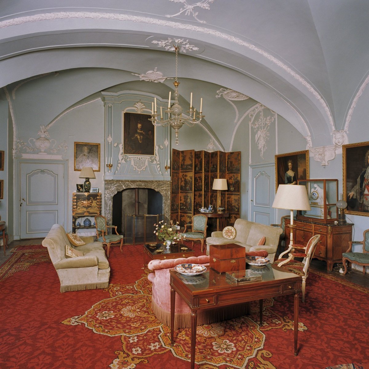 Grand castle room with white vaulted ceilings, fireplace, antique furniture, red carpet, and chandelier