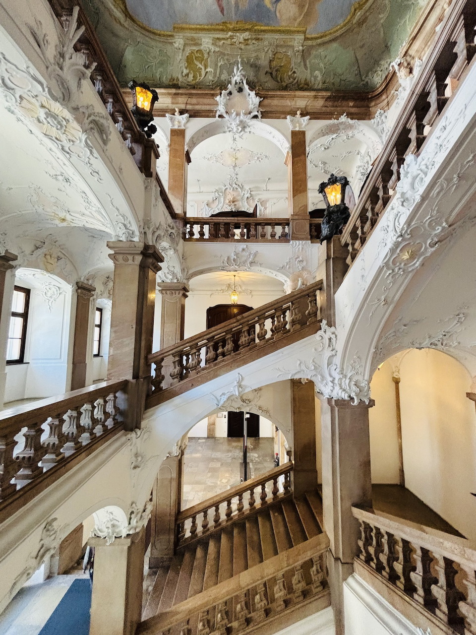 Ornate baroque staircase with white stucco decoration and wooden banisters inside Passau Dom Museum