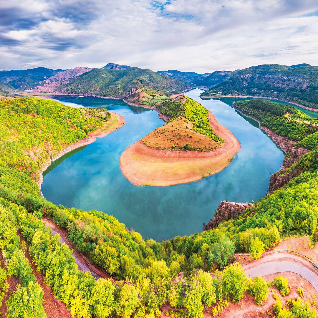 Aerial view of a curved blue river around a sandy peninsula with green hills and mountains