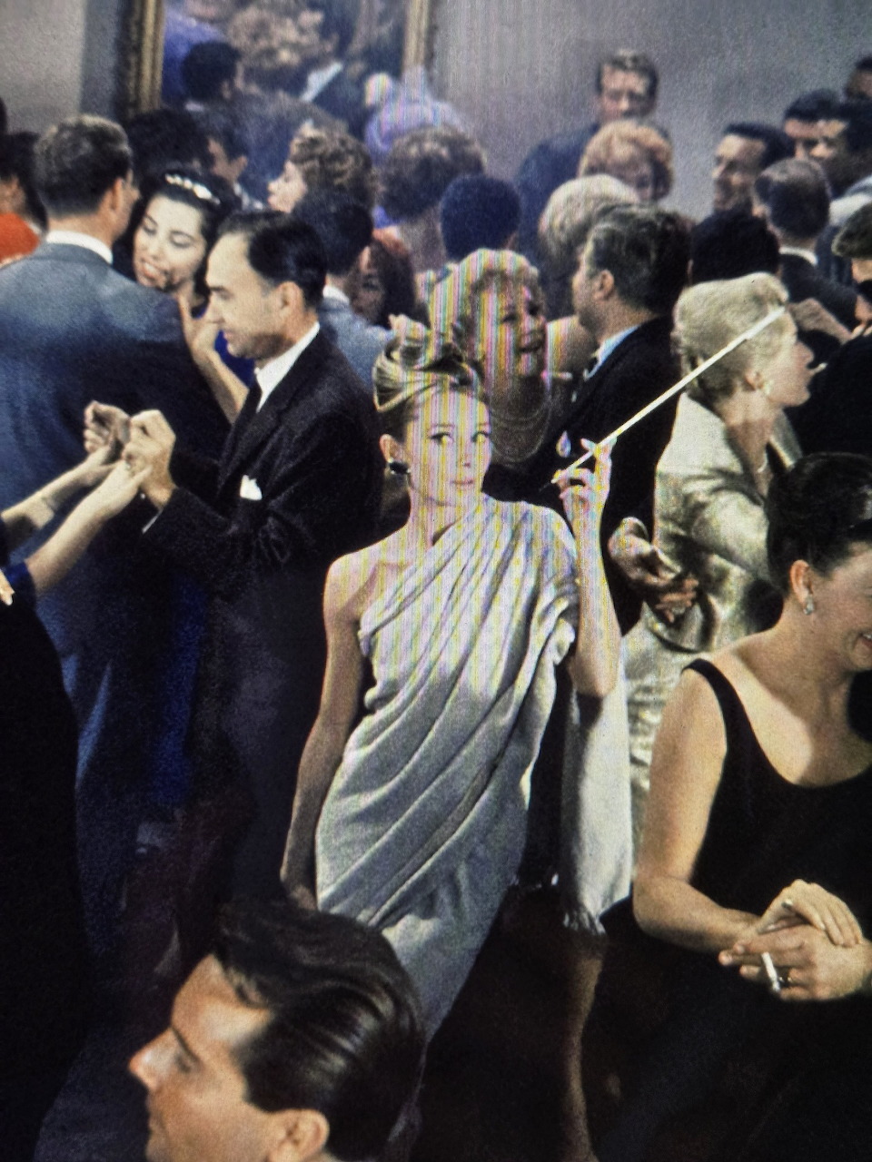 Audrey Hepburn in a white draped dress at a crowded formal party
