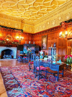 Lavish wood-paneled study room with ornate ceiling, fireplace, antique furniture, and Persian rug
