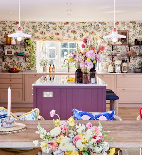 Kitchen interior with purple island, floral wallpaper, wooden table with colorful flowers, and open shelves