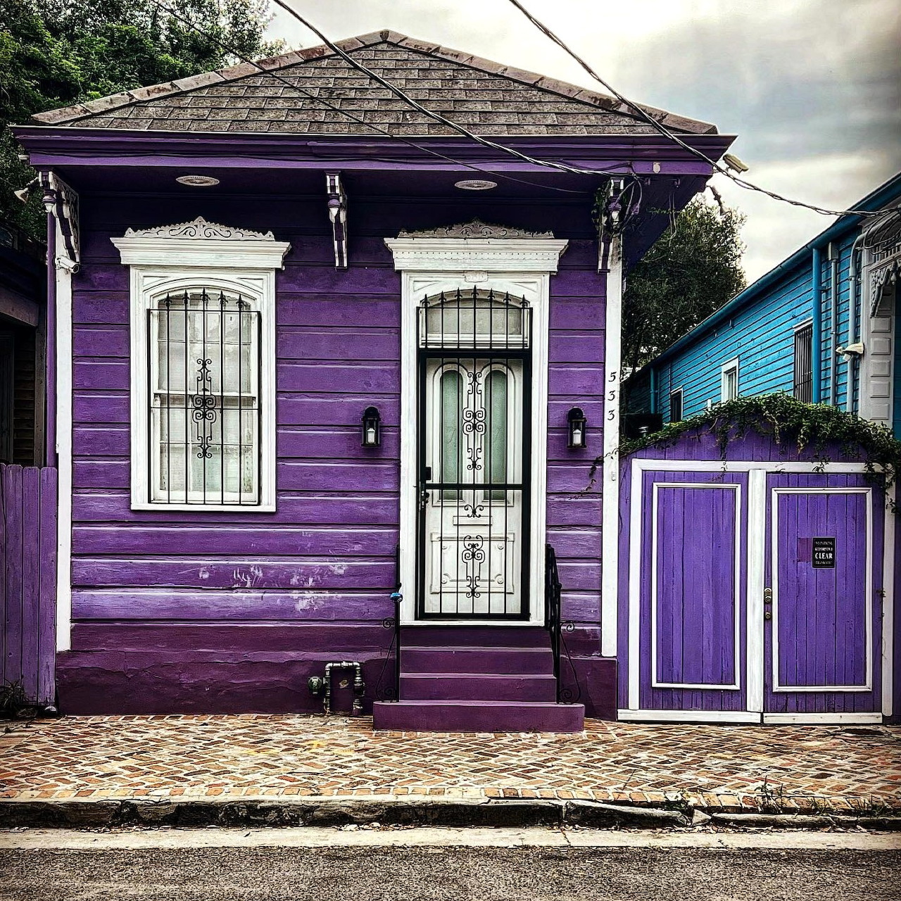 Small purple wooden house with white door and windows on urban street