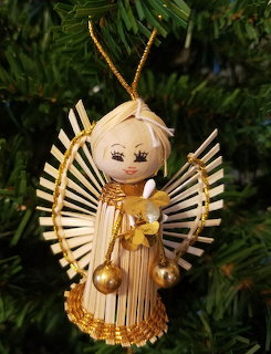 Straw angel ornament with gold trim and wings hanging on a green Christmas tree