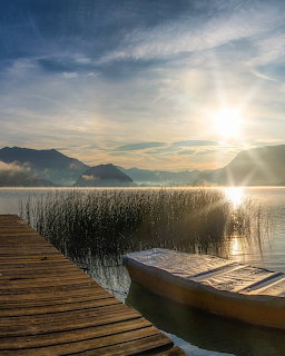 Wooden dock with canoe at sunrise on mountain lake with golden sunlight and reeds