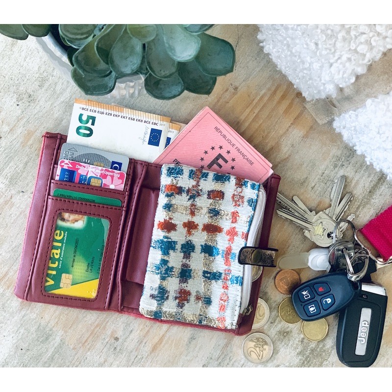 Pink wallet with money and cards beside car keys and pill organizer on textured white surface