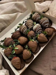 Box of chocolate-covered strawberries with decorative drizzle on a bed with white sheets