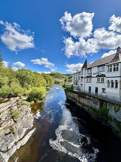 White building beside a river with trees, rocks, blue sky, and clouds
