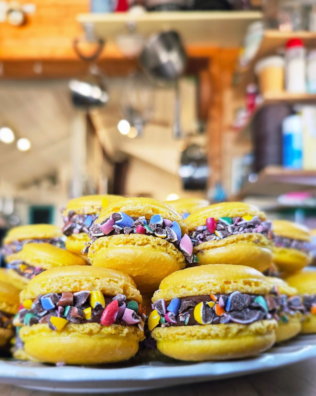Stack of yellow macarons with chocolate filling and colorful sprinkles on white plate in kitchen