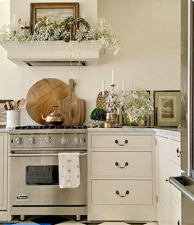 Neutral kitchen with cream cabinets, stove, wood boards, framed art, and baby's breath flowers