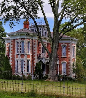 Victorian brick mansion with turret and ornate porch surrounded by trees